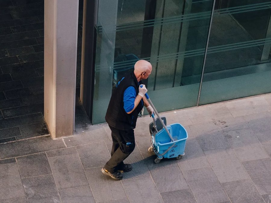 Agent d'entretien et son chariot devant un immeuble